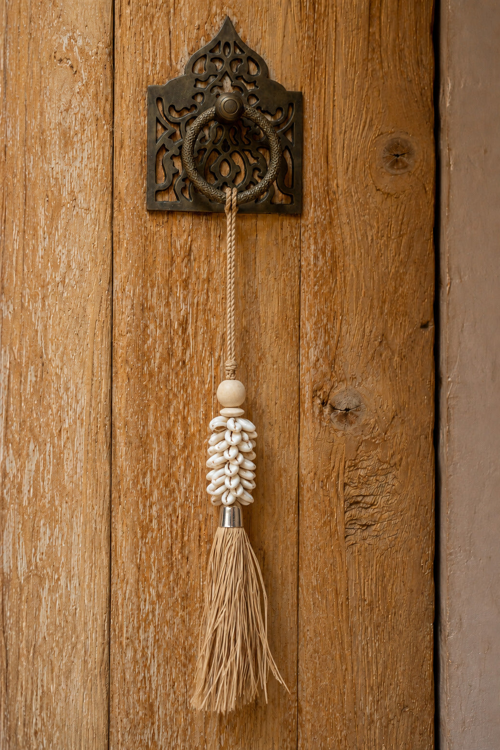 Handgefertigter Wand-Pompon aus Kaurimuscheln und Raffia Natur