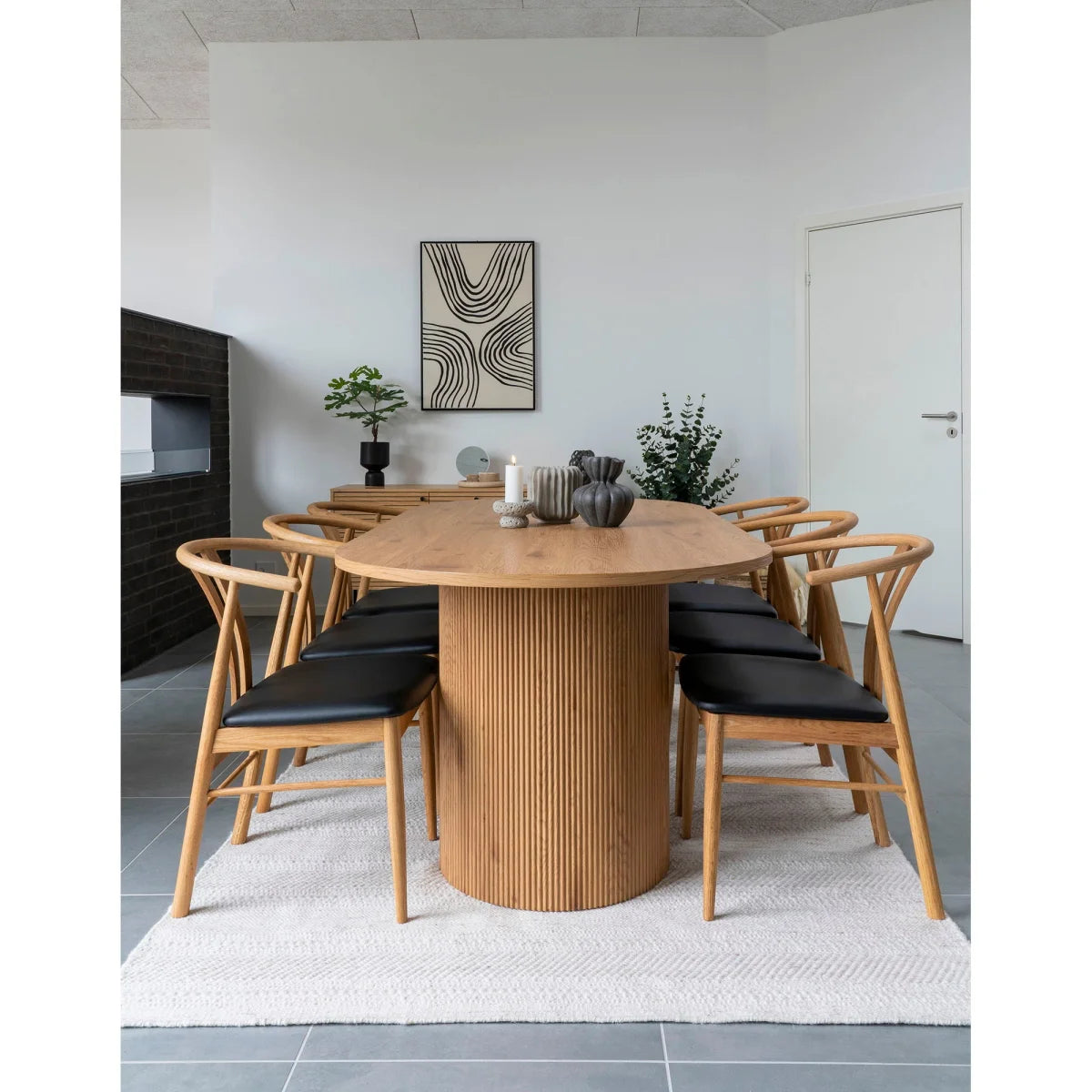 Table basse ovale en bois clair avec base cylindrique nervurée et coussins en cuir noir sur chaises assorties