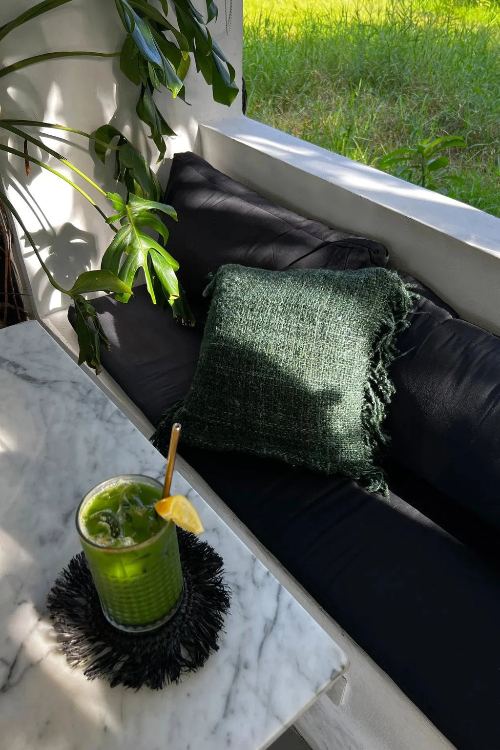 Verre vert vif avec glace, citron, paille dorée sur un dessous de verre à franges
