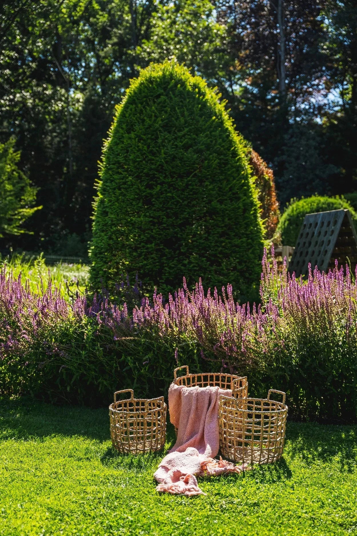 Trois paniers en rotin avec une couverture rose saumon dans un jardin coloré