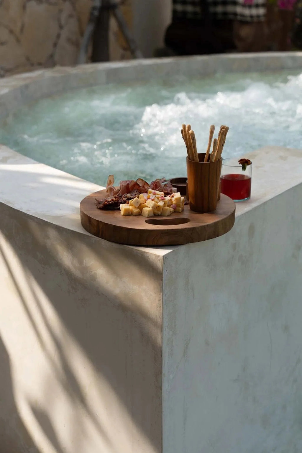 Plateau rond en racine de teck avec poignées en bois clair près d’un jacuzzi et snacks